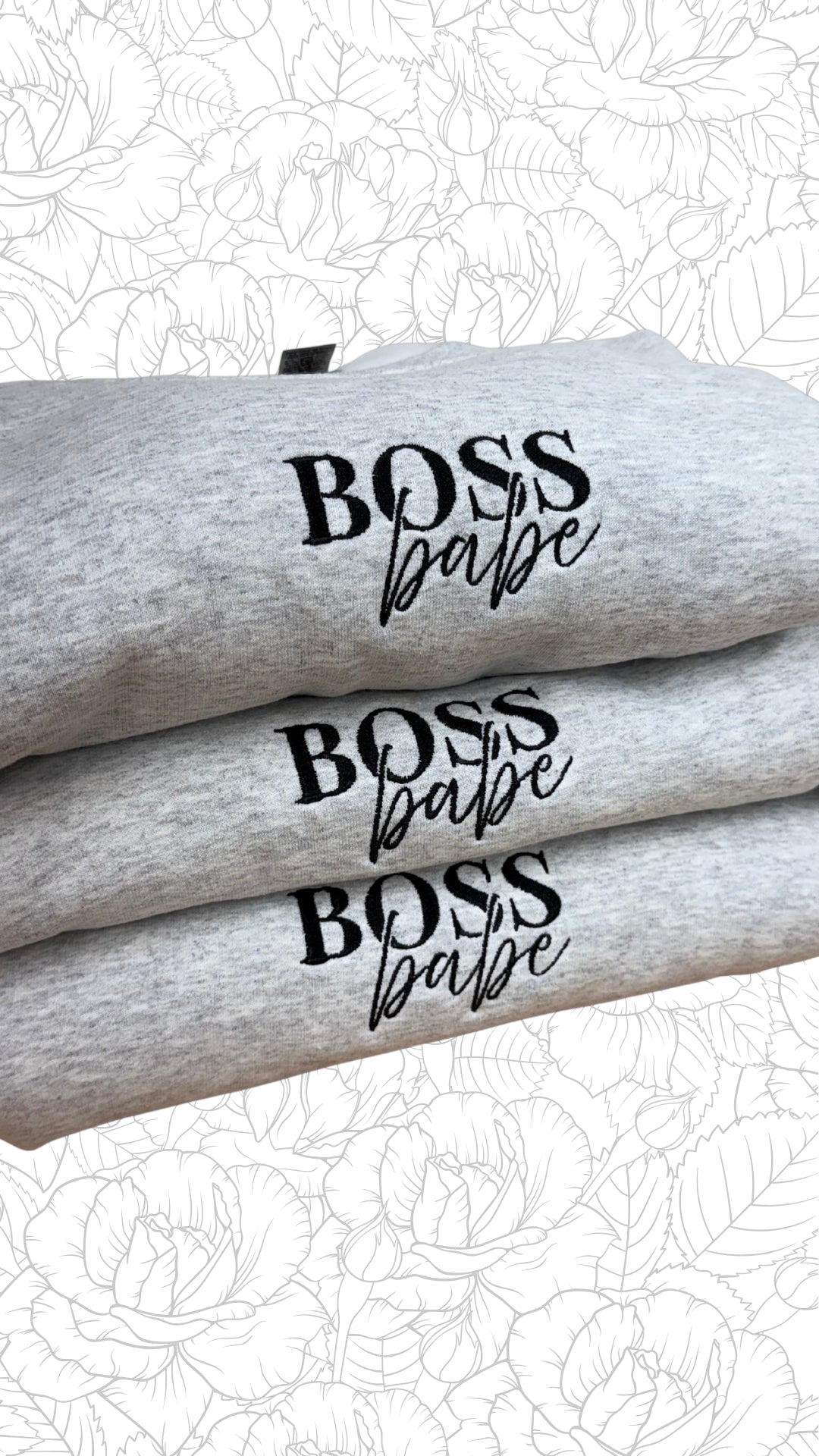 Stack of gray sweatshirts with 'BOSS babe' text on a floral patterned background