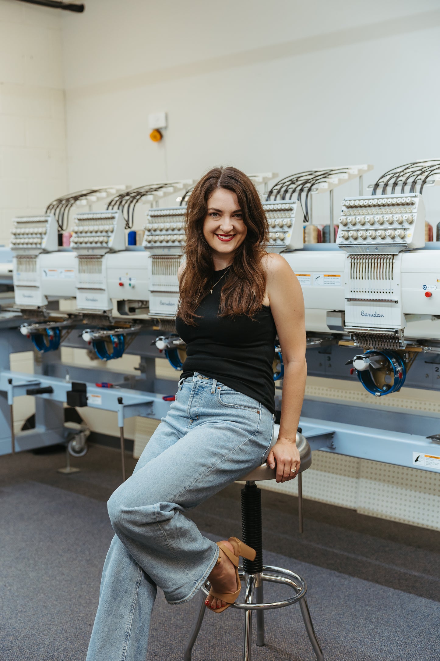 Woman sitting on a stool in a room with embroidery machines