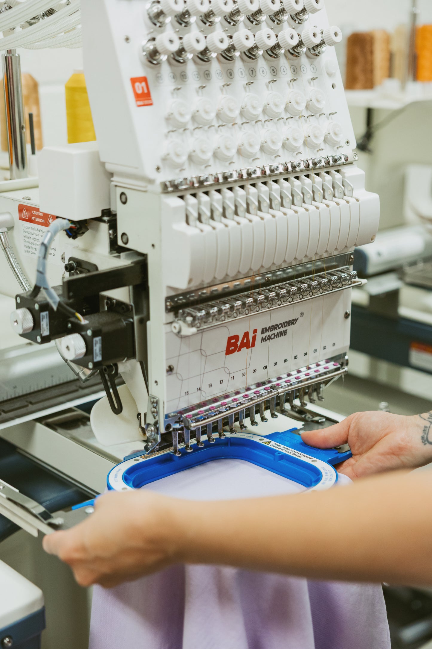 Embroidery machine with a person's hand interacting with it, likely adjusting or operating.