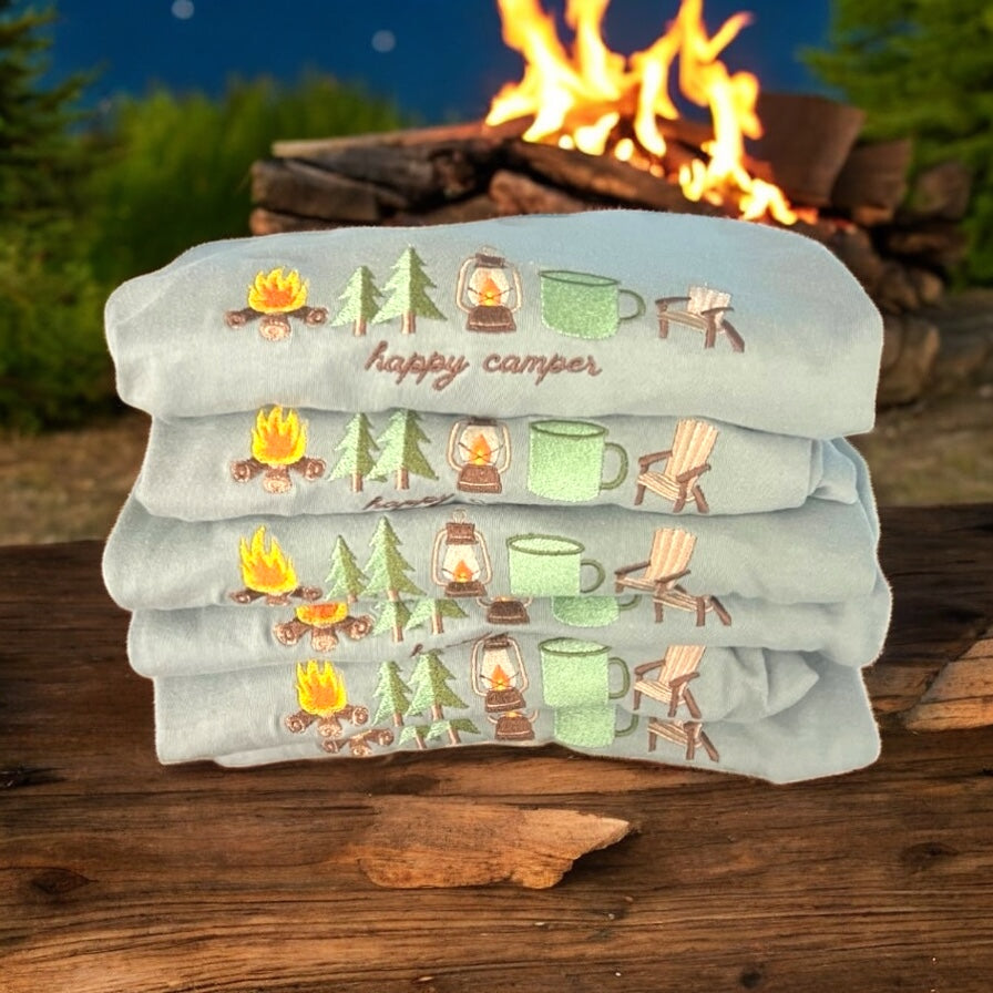 Stack of tee shirts with camping-themed designs in front of a campfire