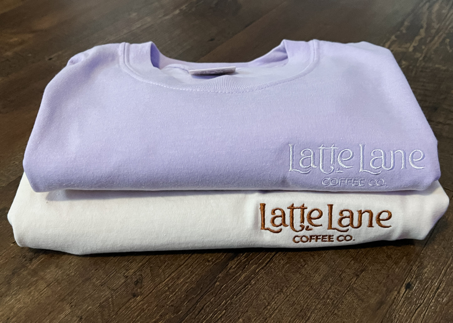 Folded shirts with 'Latte Lane Coffee Co.' branding on a wooden surface