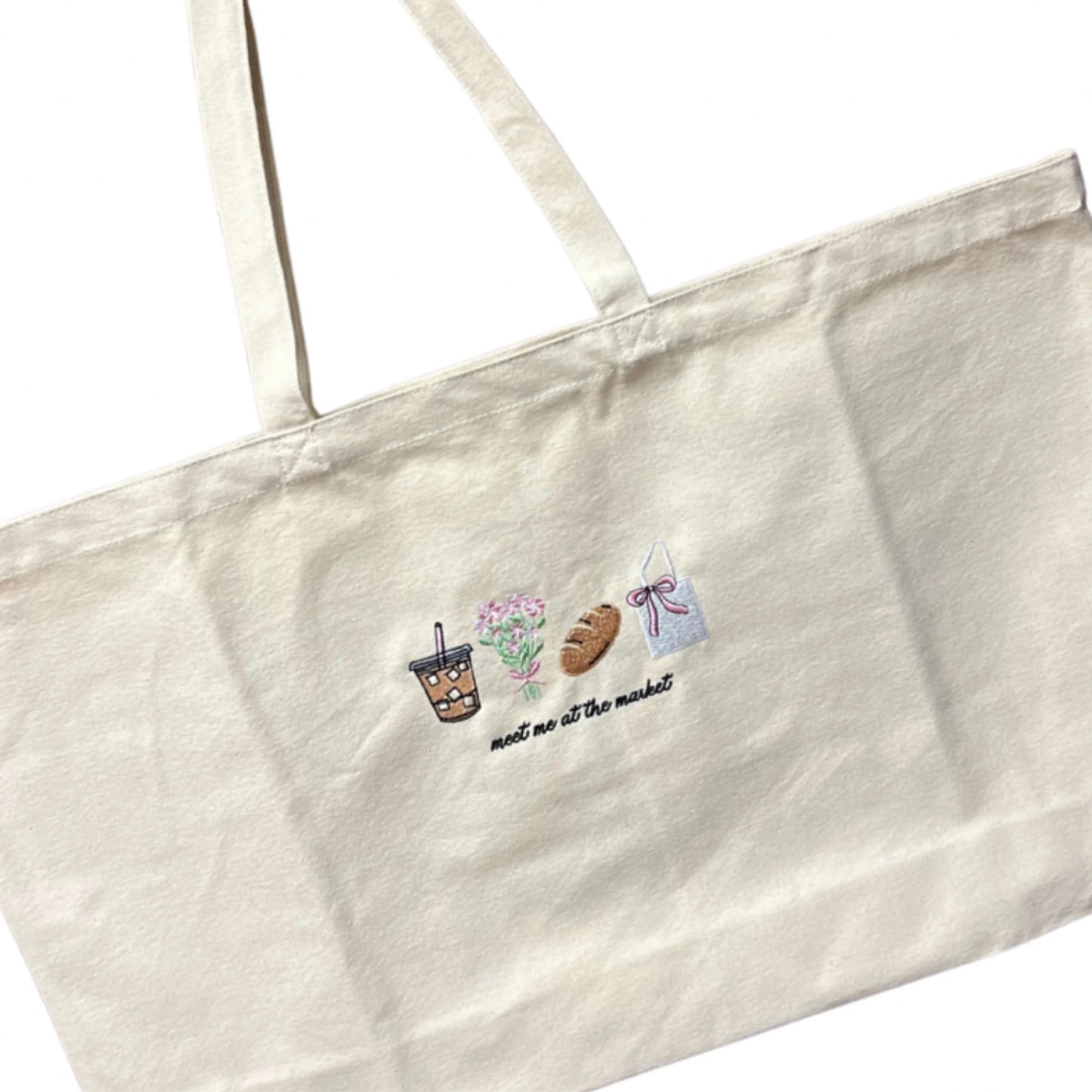 Beige tote bag with embroidered designs and text on a white background