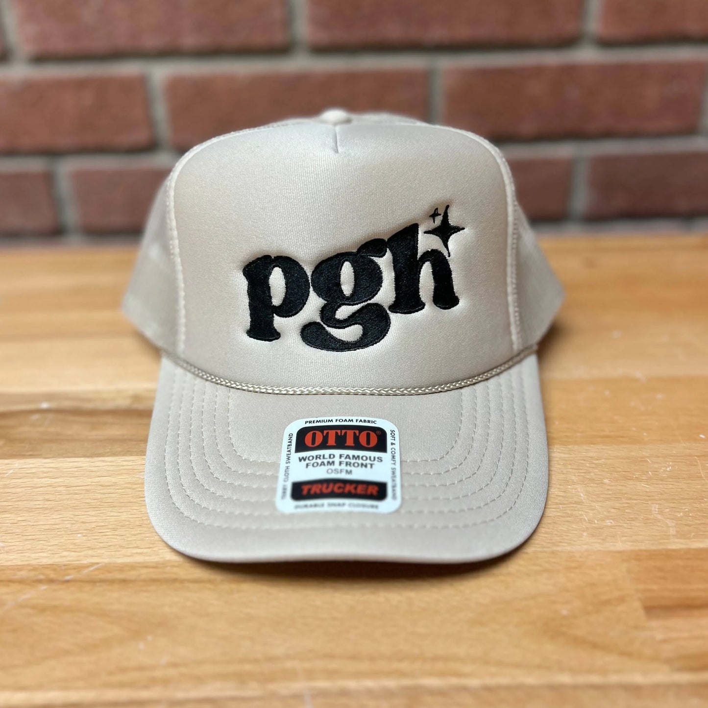 Beige cap with 'pgh' logo on a wooden surface with brick wall background
