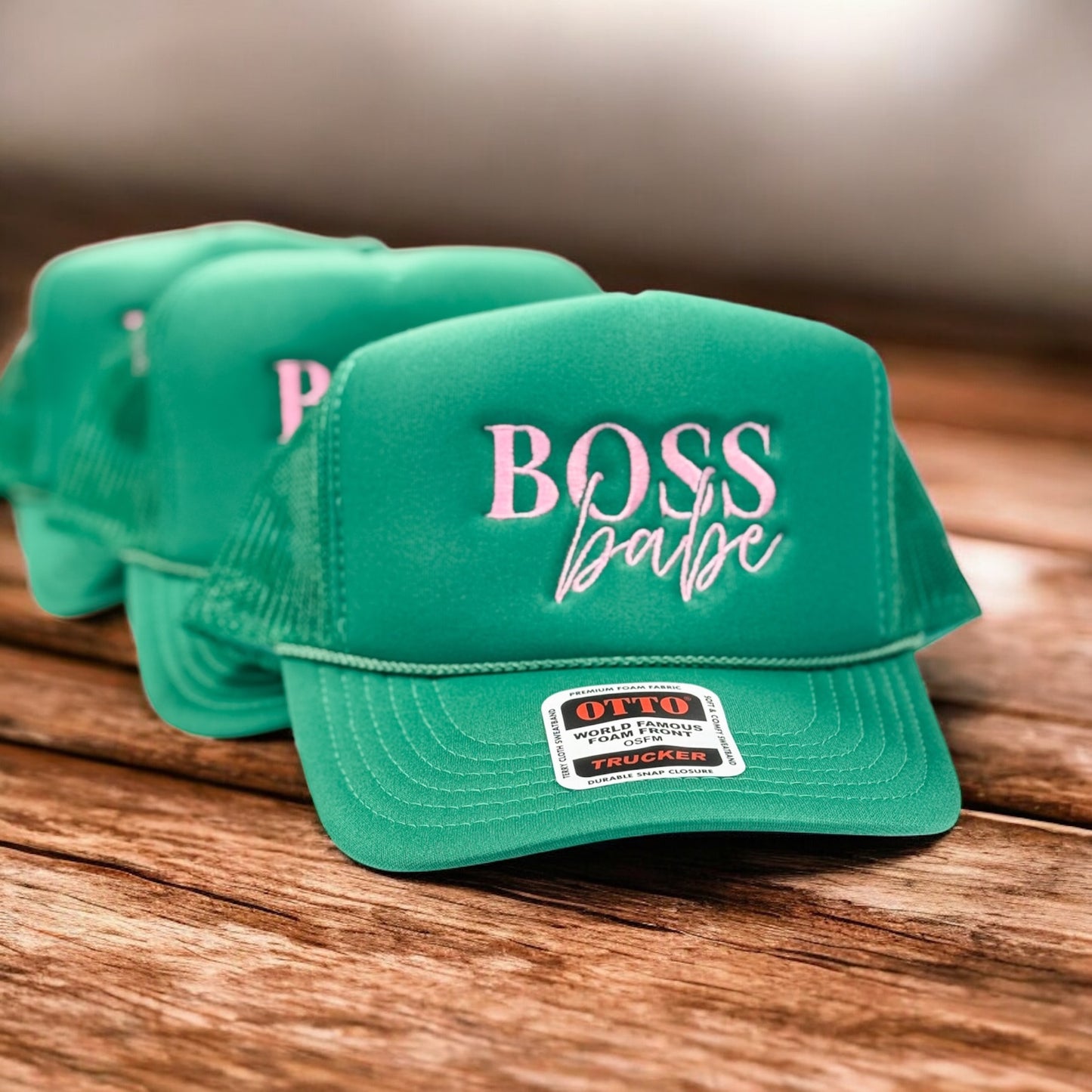 Green trucker hats with 'BOSS babe' text on a wooden surface