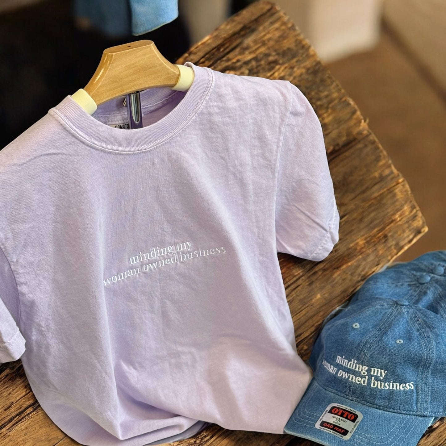 Light purple t-shirt with text and blue cap on a wooden surface