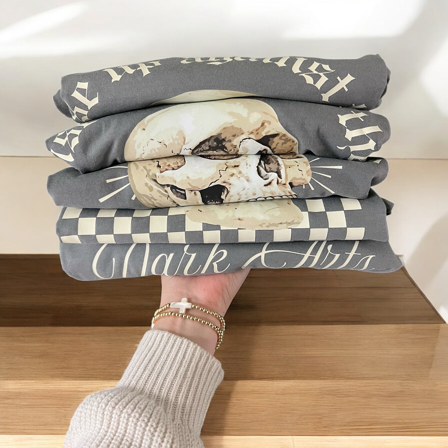 Stack of folded shirts with text and graphics held by a person on a wooden surface.