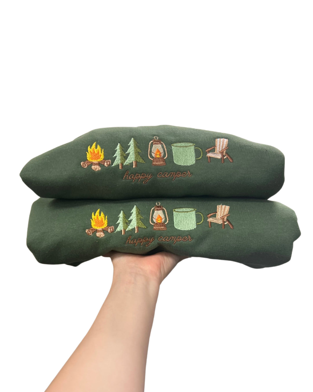 Green crew with camping-themed embroidery held by a hand on a white background